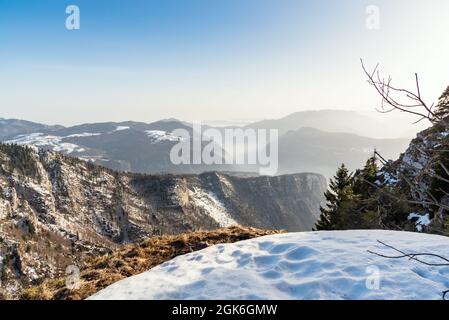 Herrliche Winterbergkulisse mit in Nebel gehüllten Tälern, die von der Spitze eines Berges in den Alpen bei Sonnenuntergang gesehen werden Stockfoto