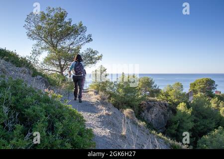 Wanderer gehen auf einem schmalen Pfad, der in einem Wald am Meer auf den Klippen von Maro Cerro Gordo ist Stockfoto