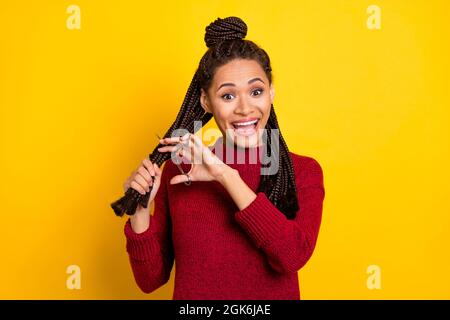 Foto von beeindruckt charmante dunkle Haut Frau gekleidet roten Pullover schneiden Dreadlocks lächelnd isoliert gelbe Farbe Hintergrund Stockfoto