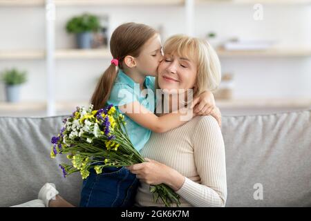 Kleines Mädchen küssen und begrüßen Frau mit Blumen Stockfoto