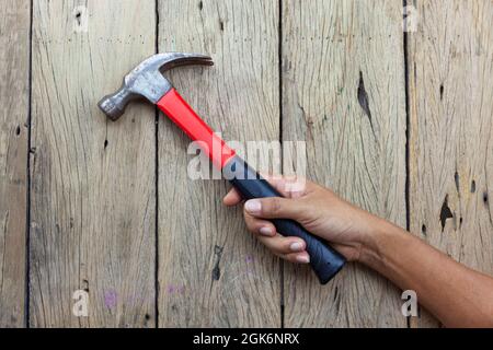 Zimmermann Hand hält Hammer auf alten Holztisch Hintergrund. Stockfoto