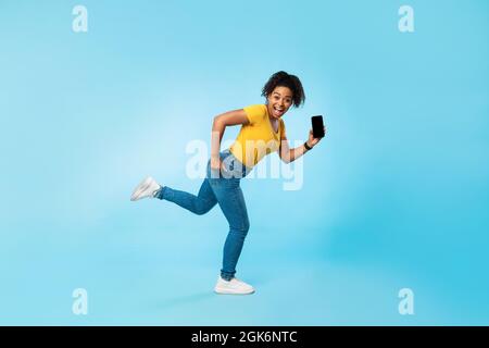 Glückliche junge Afro-Frau mit leerem Smartphone auf blauem Hintergrund, Mockup für Website oder mobile App Stockfoto