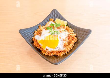 Quadratisches Tablett mit gebratenem Nasi-Gore-Reis mit Ei und köstlichem Eigelb mit Petersilie, Stück Limette auf Holztisch Stockfoto