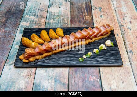 Spanischer Torrezno mit Techno-emotionalem Kochstil auf einem Bett aus Kartoffelpüree und Pommes Frites Stockfoto