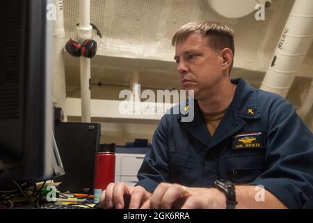 210818-N-CW176-1055 ARABIAN SEA (AUG 18, 2021) – Lt. Cmdr. Carl Muehler, ein Marinekaplan, bearbeitet Verwaltungsdokumente in der Bibliothek an Bord des Flugzeugträgers USS Ronald Reagan (CVN 76) im Arabischen Meer, August 18. Ronald Reagan wird in den Einsatzbereich der 5. US-Flotte eingesetzt, um Marineinteraktionen zu unterstützen, um die maritime Stabilität und Sicherheit in der Zentralregion zu gewährleisten und das Mittelmeer und den Pazifik durch den westlichen Indischen Ozean und drei strategische Engpässe zu verbinden. Stockfoto