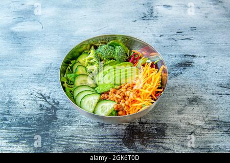 Edelstahlschüssel gefüllt mit vegetarischen Speisen auf blauem Holztisch. Stockfoto