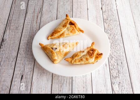 Drei nicht geschlossene argentinische Rindfleisch-Empanadas in weißem Teller auf weißem Holztisch Stockfoto