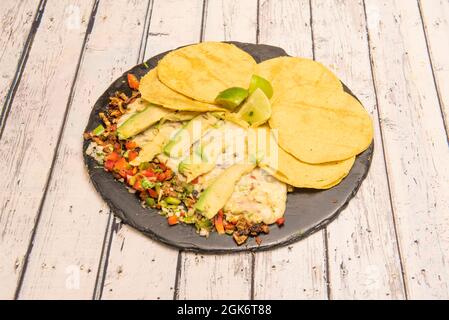 Kombiniertes mexikanisches Gericht aus Rinderdraht mit Scheiben Avocado, sautiertem Gemüse, kleinen Maistortillas und Kalkstücken Stockfoto