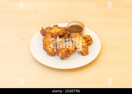 Hähnchenflügel mit Grillsauce auf weißem Teller und Holztisch Stockfoto