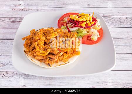 Kolumbianischer Stil, geschreddertes Fleisch arepa, garniert mit Mais- und Tomatensalat auf einem weißen Teller Stockfoto