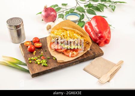 Arepa llanera mit geschreddertem Rindfleisch, Avocado, Tomaten, Cheddar-Käse und anderen Gewürzen auf Holzbrett Stockfoto