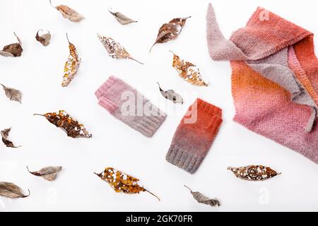 Herbstkomposition. Strickschal und Fäustlinge, Herbstblätter auf weißem Hintergrund. Flach liegend, Draufsicht. Gemütliches Zuhause Konzept Stockfoto