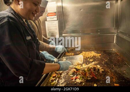 210819-N-YP246-1094 OSTCHINESISCHES MEER (AUG 19, 2021) Engineman 1st Class Larissa Guarino (links) und Culinary Specialist 2nd Class Allen Sarcos Mann der Grill während einer mongolischen Nacht veranstaltet von der First Class Petty Officer Association an Bord des Amphibientransportschiffes USS Green Bay (LPD 20). Green Bay, Teil des Amphibiengeschwaders 11, ist im Verantwortungsbereich der 7. US-Flotte tätig, um die Interoperabilität mit Verbündeten und Partnern zu verbessern und als einsatzbereite Einsatztruppe für den Frieden und die Stabilität in der Indo-Pazifik-Region zu dienen. Stockfoto