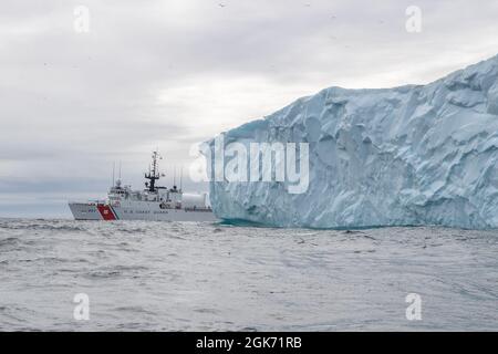 LABRADOR SEA -- (Aug 19, 2021) die USCGC Escanaba (WMEC 907) durchfährt einen Eisberg in der Labradorsee. Die Fräser sind in der Region am Ende der warmen Jahreszeit in Betrieb, wodurch das Risiko reduziert wird. Die Escanaba ist ein 270 Meter langer, berühmter Mittelausdauerschneider mit einer Besatzung von rund 100 Personen und führt Missionen durch, die die Sicherheit im Seeverkehr und die Strafverfolgung betonen Stockfoto