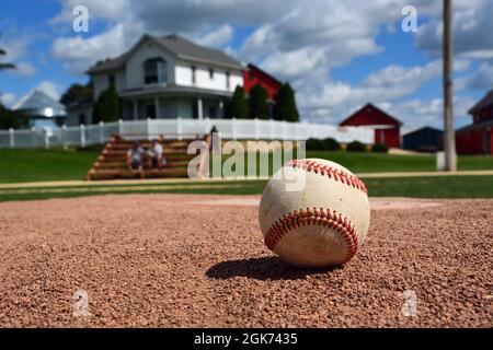 Ein Baseballspiel sitzt auf dem Pitchers-Hügel beim ehemaligen Filmset von Field of Dreams in Dyersville, Iowa. Der Fokus liegt auf dem Baseballspiel. Stockfoto