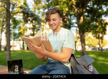 Bildungskonzept. Teenager-Student Kerl Buch im Freien lesen und Vorbereitung auf Prüfungen, sitzen auf dem Campus Stockfoto