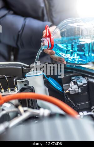 Der männliche Fahrer gießt Frostschutzmittel in den Tank, um die Windschutzscheibe zu sprühen. Stockfoto