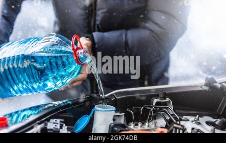 Der männliche Fahrer gießt Frostschutzmittel in den Tank, um die Windschutzscheibe während eines Schneesturms zu sprühen. Stockfoto