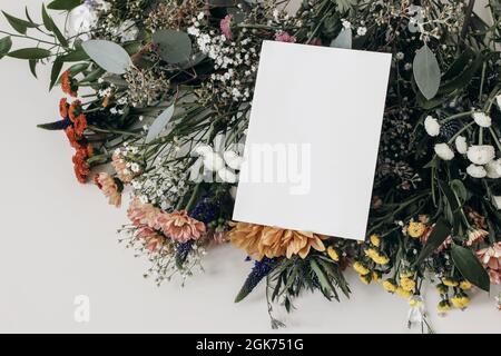Moody feminine Hochzeit, Geburtstag Mockup Szene. Grußkarte aus leerem Papier, Einladung auf Blumenstrauß. Gypsophila und bunte santini Mütter mit Stockfoto