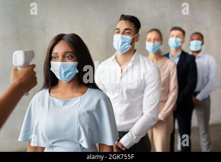 Person Mit Berührungslosem Thermometer, Das Die Temperatur Für Eine Gruppe Von Arbeitern In Masken Überprüft Stockfoto