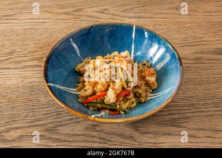 In einer wunderschönen blauen Schüssel sautierten Reis im asiatischen Stil mit Garnelen, Gemüse, Mohnsamen und Sojasauce Stockfoto