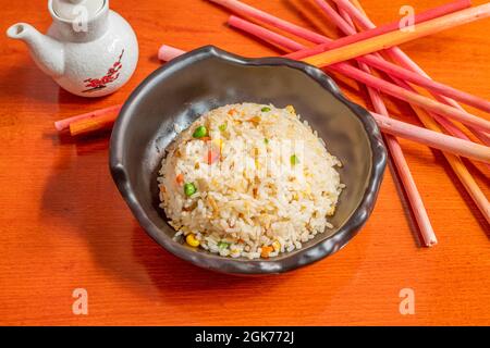 Schwarze Schüssel gebratenen Reis mit verschiedenen Gemüsesorten, Sojasauce in einem Glas und Orangenholz Hintergrund Stockfoto