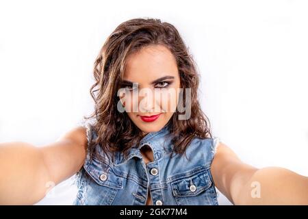 Selfie-Manie. Junge attraktive Frau mit braunem Haar und einem Jeans-Outfit, die ein Selfie macht. Intensiver Blick, unterstrichen durch das Make-up der Augen. Stockfoto