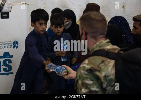 Ein Fallschirmjäger der 82. Airborne Division übergibt einem afghanischen Kind während einer nicht kämpferischen Evakuierungsoperation auf dem Ali Al Salem Airbase, Kuwait, 23. August 2021 eine Flasche Wasser. Stockfoto