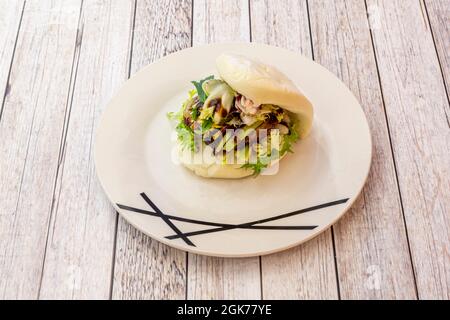 Weißer Teller mit asiatischem Entenlende bao-Brot mit grünem Sprossalat auf weißem Tisch Stockfoto