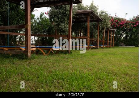 Orientalischer Pavillon aus Holz mit Ziegeldach unter hohen Bäumen vor Gebäuden mit keramischen Ziegeldach in einem wunderschönen öffentlichen Park. Hoher pH-Wert Stockfoto