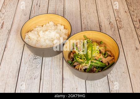 Schüssel mit philippinischer bicol Fleisch mit Gemüse und garniert mit weißem Reis auf weißem Tisch Stockfoto