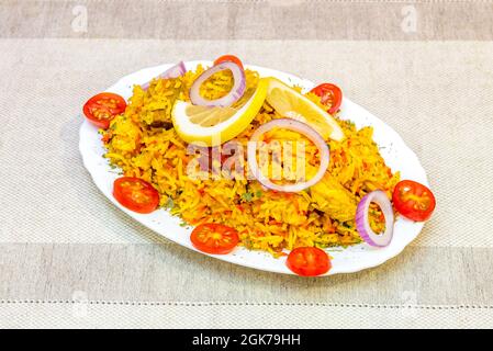 Atemberaubendes Biryani-Rezept für indischen Reis, serviert auf einem Tablett mit Kirschtomaten, roten Zwiebelringen und Zitronenarnish Stockfoto