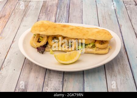 Gebratenes paniertes Tintenfisch-Sandwich mit Salat und Zitronenverband auf weißem Teller Stockfoto