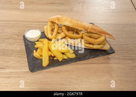 Sandwich aus Tintenfischringen, zerschlagen mit Mehl und Ei, Mayonnaise-Sauce und Pommes Frites Stockfoto