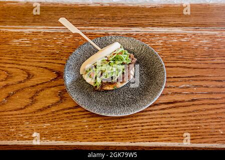 Asiatisches Lammsandwich mit Teriyaki-Sauce auf grauem Teller auf dunklem Holztisch. Stockfoto