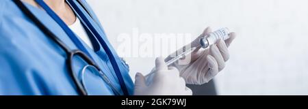 Teilansicht des Arztes in Latexhandschuhen, die Spritze mit Impfstoff füllen, Banner Stockfoto