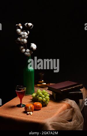 Stillleben mit Früchten und Büchern in dunkler Umgebung. Vasen, Becher und Tüll Stockfoto