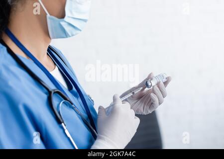 Beschnittene Ansicht des Arztes in einer Spritze mit medizinischer Maskenfüllung und Impfstoff Stockfoto