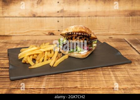 Entenfleisch-Burger mit karamellisierten Zwiebeln, Salat, Mayonnaise, Ziegenkäse und Grillsauce mit Beilagen Stockfoto