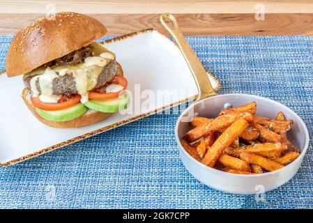 Rinderburger mit karamellisierter Zwiebel und Avocado garniert mit Süßkartoffeln auf blauer Tischdecke Stockfoto