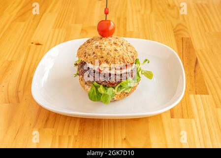 Burger mit Samenbrot, darauf punktierte Kirschtomate, Lammsalatsprossen, Zwiebel- und Tomatenmarmelade, mariniertes und gehacktes Rindfleisch und einem Stück Ziegenlauch Stockfoto