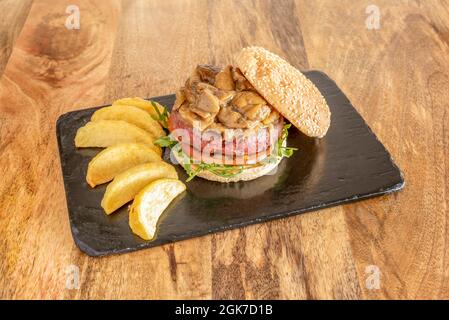 Kalbsburger mit seltenem Fleisch mit Zwiebeleintopf und Pilzen auf der Oberseite, Tomatenscheibe und Rucola und einigen Pommes frites in einem Fächer angeordnet Stockfoto