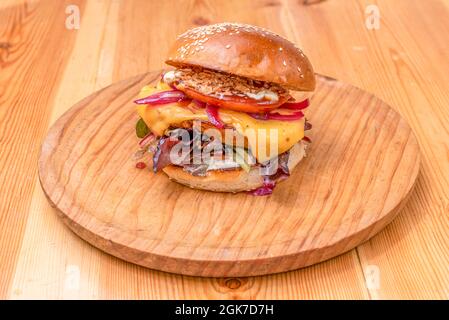 Double Beef Burger mit geschmolzenem Cheddar-Käse, karamellisierten roten Zwiebeln, Eichensalat, Tomatenscheiben, knusprigen Zwiebeln, Mayonnaise und Ketchup auf einem hölzernen pla Stockfoto