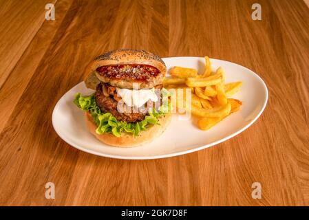 Rindfleisch-Burger mit einem Stück Gänseleberpastete am Rand, Salat, Sauce, karamellisierter Zwiebel und Beilage-Pommes Stockfoto