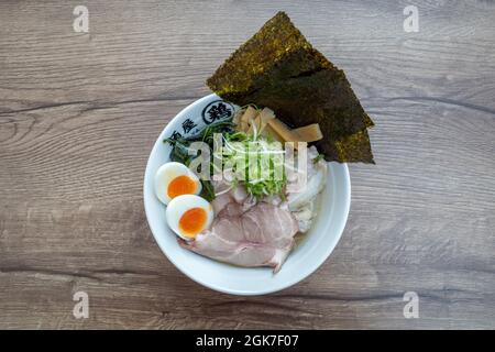 Shio Ramen, japanische Nudellattenmuscheln-Suppe, darauf Schweinefleisch, gekochtes Ei, Bambussprossen, rote Zwiebel und Nori, auf einem hölzernen Außentisch. Stockfoto