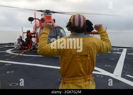 Ens. Ryan Dunkle, ein Crewmitglied der Küstenwache, Healy (WAGB 20), sendet Signale an ein Betankungsteam, während es während des gemeinsamen Flugtrainings vor der Küste Alaskas während des Einsatzes von Healy in der Arktis am 25. August 2021 einen Hubschrauber der Air Station Kodiak MH-65 Dolphin betankt. Die Landeanzeiger sind für die Kommunikation mit der Flugbesatzung und den Cutter-Besatzungsmitgliedern während des Flugbetriebs verantwortlich. Stockfoto