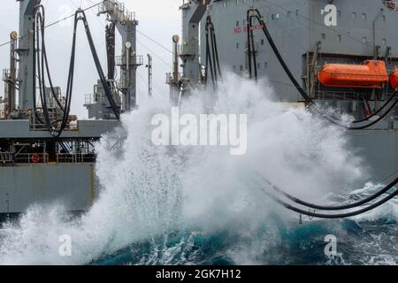 210826-N-DW158-1200 ARABIAN SEA (AUG 26, 2021) – Wellen stürzen gegen den militärischen Sealift Command Fleet Replenishment Oiler USNS Pecos (T-AO 197) während eines Replenishment-at-Sea mit dem Flugzeugträger USS Ronald Reagan (CVN 76), nicht abgebildet, im Arabischen Meer, 26. August. Ronald Reagan ist das Flaggschiff der Carrier Strike Group 5 und wird im Einsatzgebiet der 5. US-Flotte zur Unterstützung von Marineoperationen eingesetzt, um die maritime Stabilität und Sicherheit in der Zentralregion zu gewährleisten. Verbindung des Mittelmeers mit dem Pazifik durch den westlichen Indischen Ozean und drei strategische Engpässe. Stockfoto