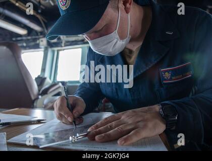 PHILIPPINISCHES MEER (Aug 26, 2021) LT. j.g. Brandon Parmely aus Austin, Texas; bereitet während MALABAR 2021 ein Manövrierbrett im Pilothaus des Arleigh Burke-Klasse-Lenkflugkörper-Zerstörers USS Barry (DDG 52) vor. Barry ist derzeit im Einsatz und unterstützt Commander, Task Force 71 (CTF 71)/Destroyer Squadron 15 (DESRON 15), die größte vorwärtseingesetzte DESRON der Marine und die wichtigste Surface Force der 7. US-Flotte. Stockfoto