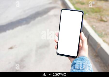Mockup Bild der Frau halten weißen Desktop-Bildschirm Handy im Freien. Verschwommene Asphaltstraße im Hintergrund. Stockfoto