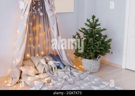 Stilvolles, modernes Kinderzimmer. Kinderbett mit Markise. Weihnachtsbaum in einem Korbkorb. Einrichtung im skandinavischen Stil Stockfoto